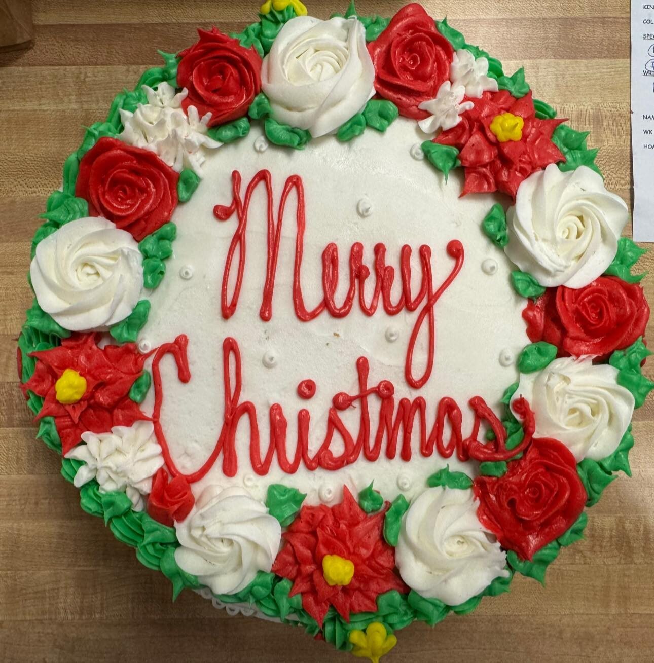 Round buttercream cake with a piped holly wreath reading Merry Christmas